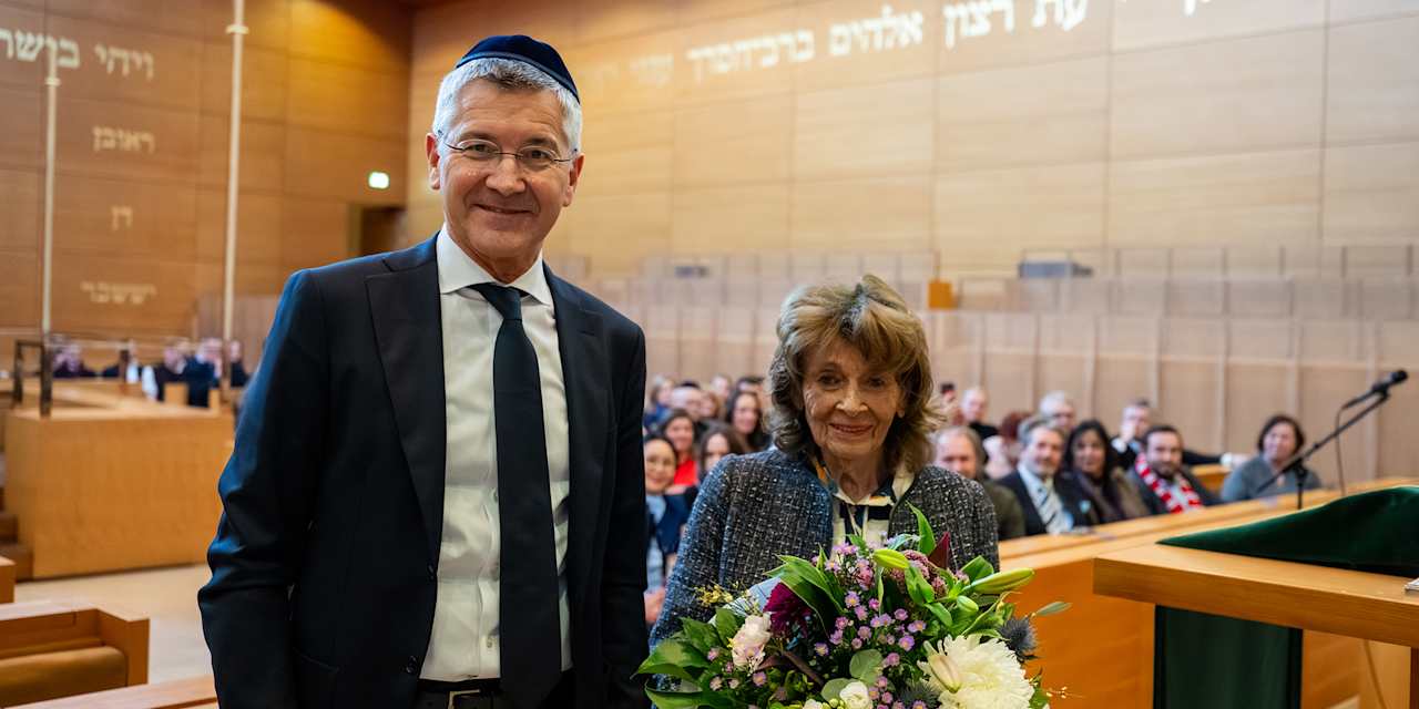 Herber Hainer und Charlotte Knobloch in einer Synagoge in München, Knobloch hält Blumen in der Hand