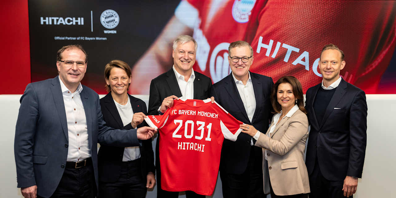 Die Verantwortlichen des FC Bayern und Hitachi Energy halten ein Trikot mit der Aufschrift 2031 in die Kamera.