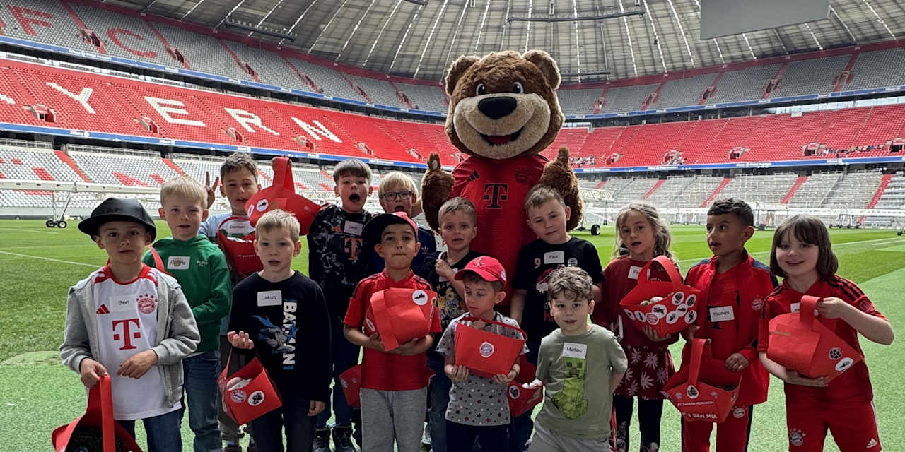 Berni und KIDS CLUB-Kinder stehen mit ihrem Osternest auf dem Rasen der Allianz Arena.
