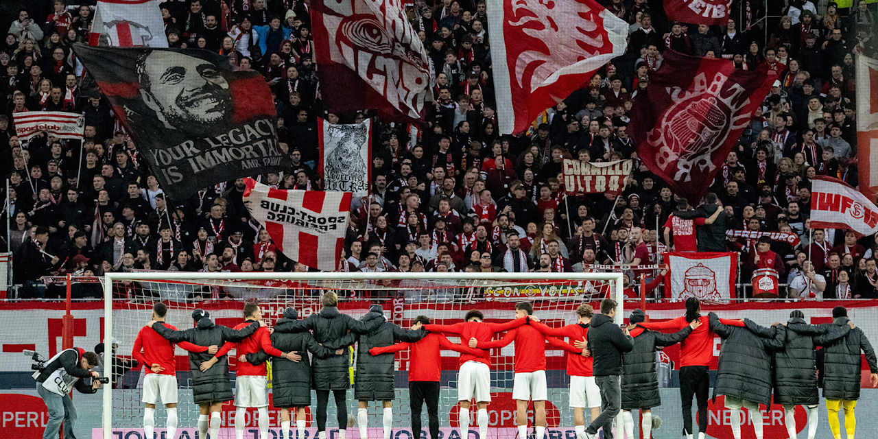 Spieler des SC Freiburg hüpfen Arm in Arm vor der Fankurve