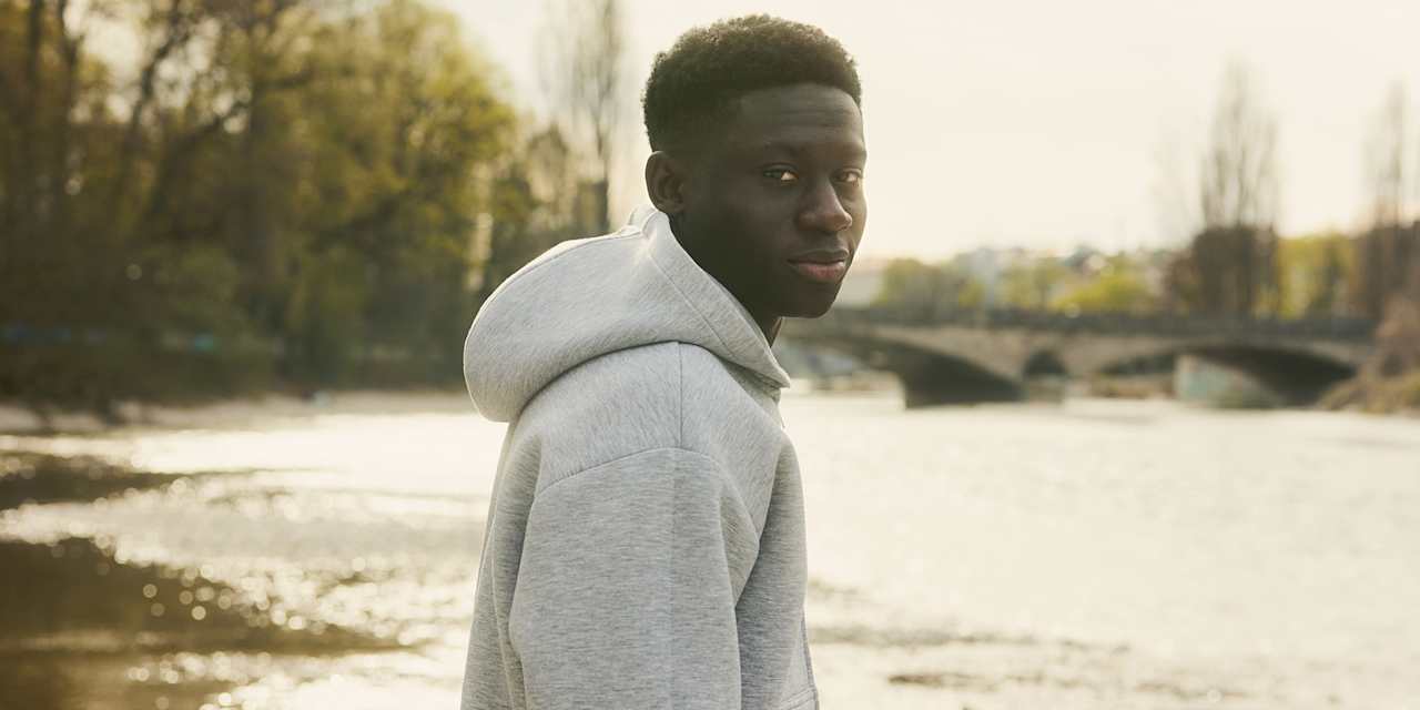 Bara Sapoko steht im grauen Hoodie an der Isar