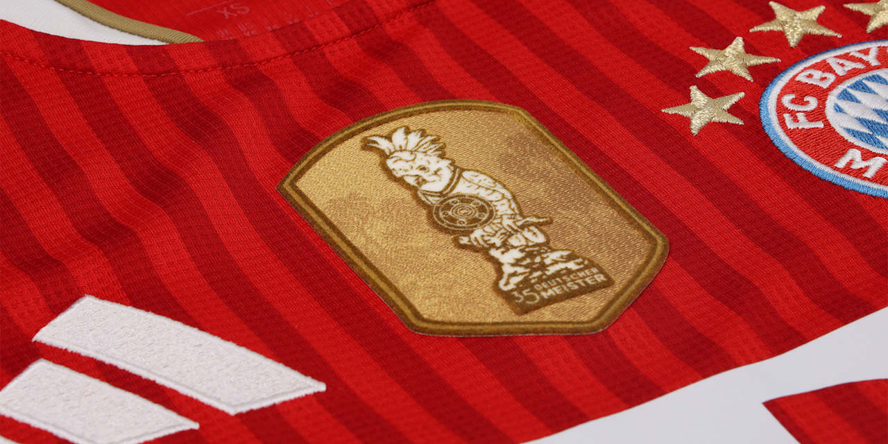 Goldenes Kakadu-Batch auf dem roten Home Trikot des FC Bayern für die Saison 2026-27