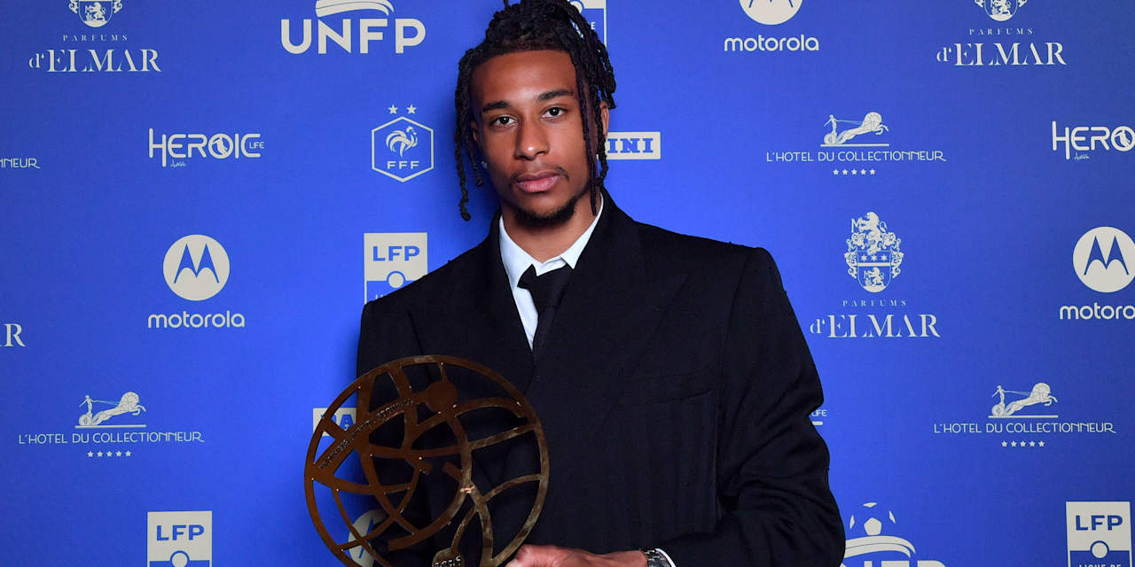 Michael Olise blickt mit Trophäe vor einem blauen Hintergrund in die Kamera