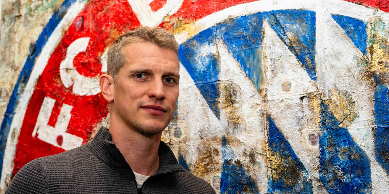 Lars Bender steht vor dem FC Bayern Logo und schaut in die Kamera.