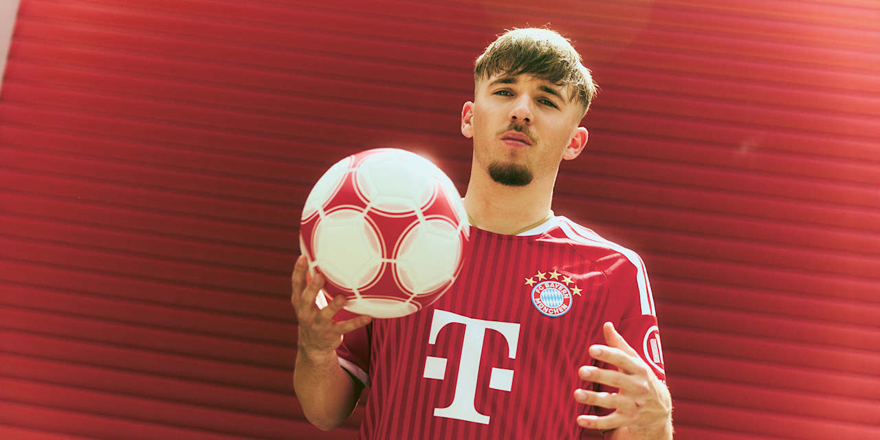 Lennart Karl steht im FC Bayern Trikot vor einem roten Tor und hält einen Ball in der Hand