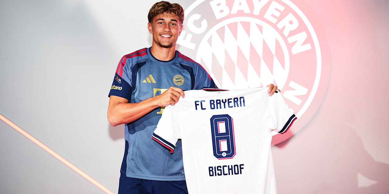 Tom Bischof hält lächelnd ein weißes Away Trikot des FC bayern mit der Rückennummer 8 Bischof hoch