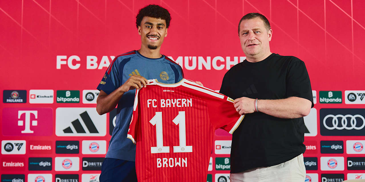 Max Eberl und Nathaniel Brown halten gemeinsam das FC Bayern Trikot mit der Nummer 11 hoch