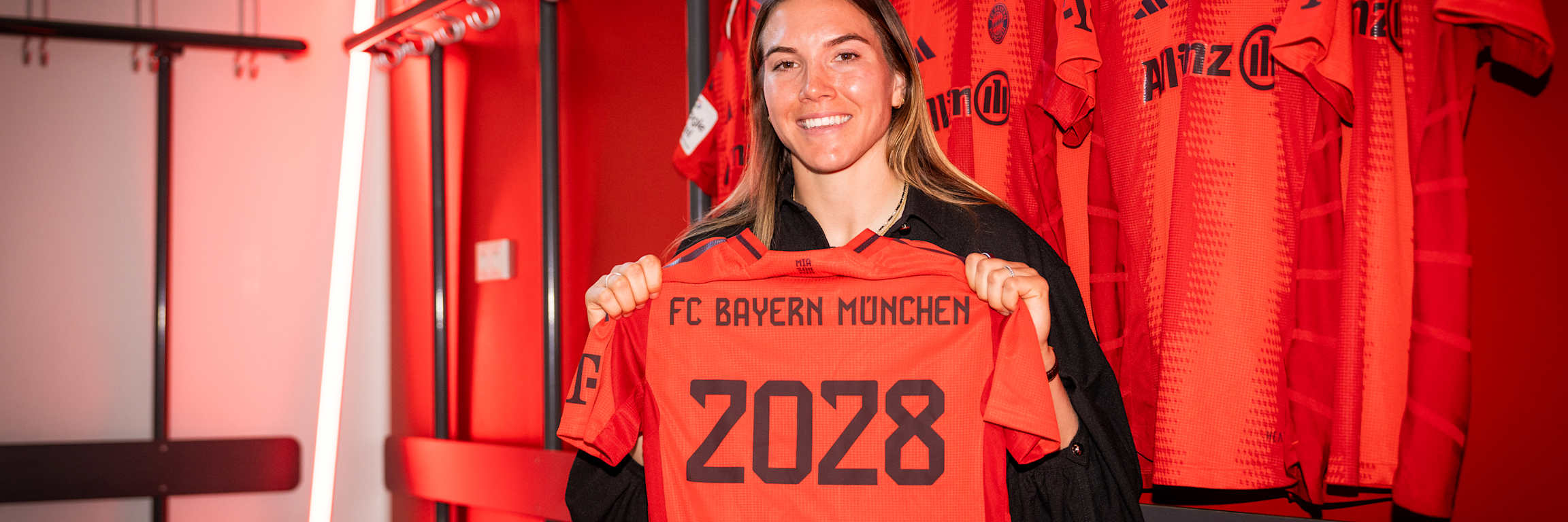 Vanessa Gilles smiles holding the FC Bayern shirt with her name and contract expiry year 2028.