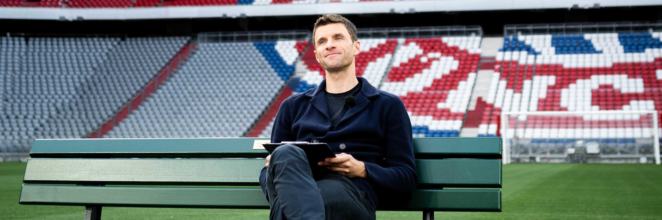 Thomas Müller sits in the Allianz Arena on a park bench on the pitch.