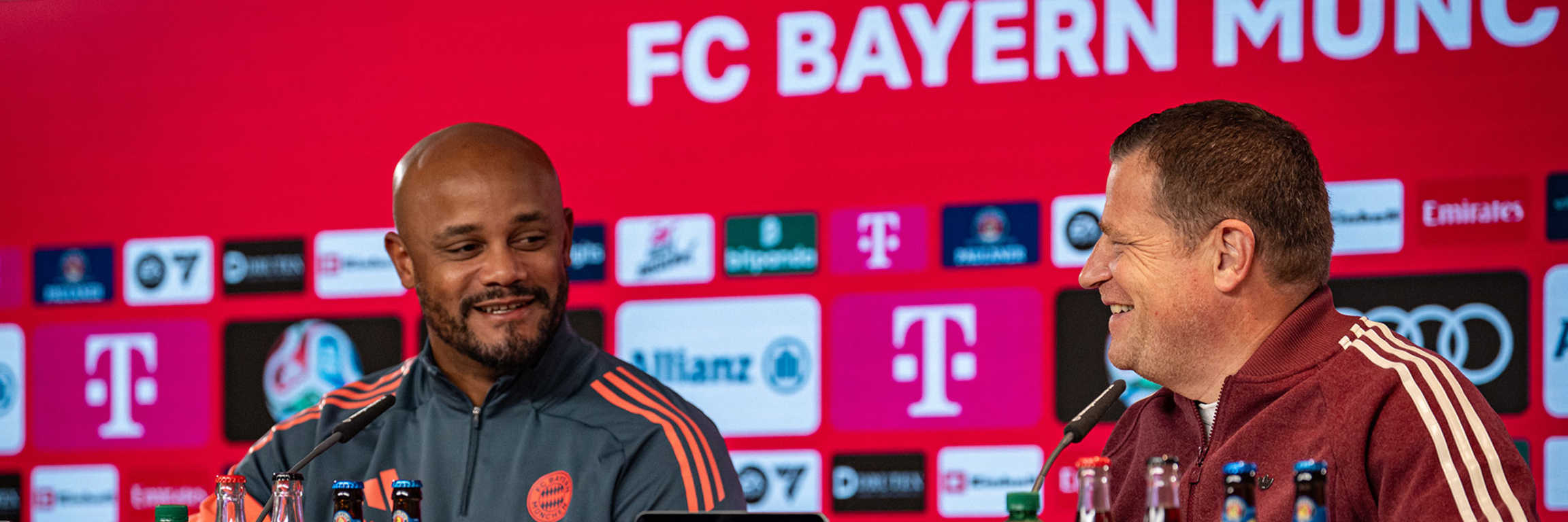 Vincent Kompany und Max Eberl schauen sich im Pressetalk des FC Bayern lächelnd an