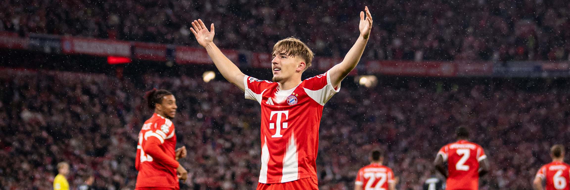 Nach seinem 1. Champions League-Tor für den FC Bayern gegen Club Brügge steht Lennart Karl mit ausgebreiteten Armen vor der Fankurve.