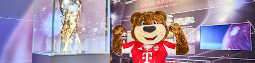 Maskottchen Berni posiert vor Pokalen im FC Bayern Museum