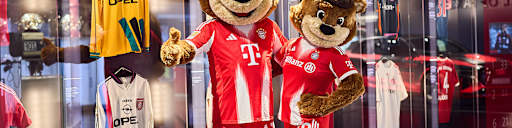 Die Maskottchen Berni und Mia posieren vor der Trikotwand im FC Bayern Museum