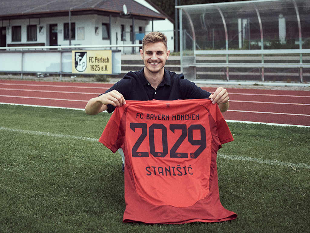 Josip Stanisic holds up an FC Bayern shirt on the pitch of his boyhood club FC Perlach.