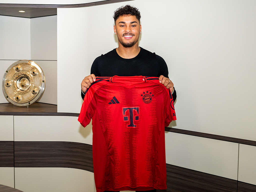 Armindo Sieb hält nach der Vertragsunterschrift ein Trikot des FC Bayern hoch.