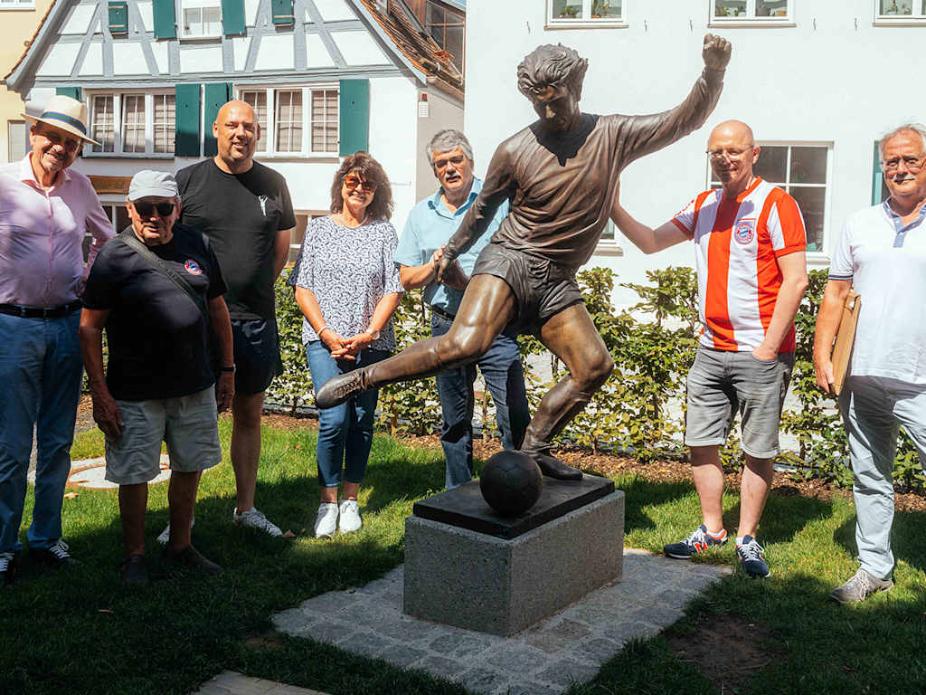 FC Bayern-Fans stehen neben der Statue von Gerd Müller in Nördlingen.