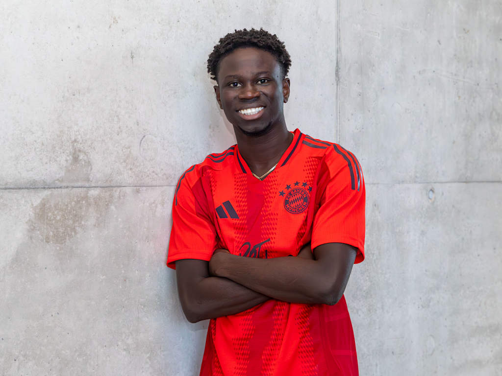 FC Bayern II new signing Bajung Darboe in the FC Bayern home jersey in front of a grey wall.