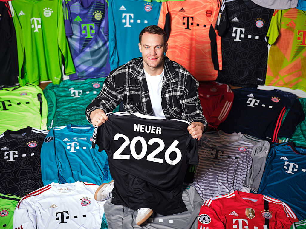 Manuel Neuer sitzt zwischen seinen Trikots des FC Bayern und hält ein Trikot mit der Neuer 2026 in der Hand