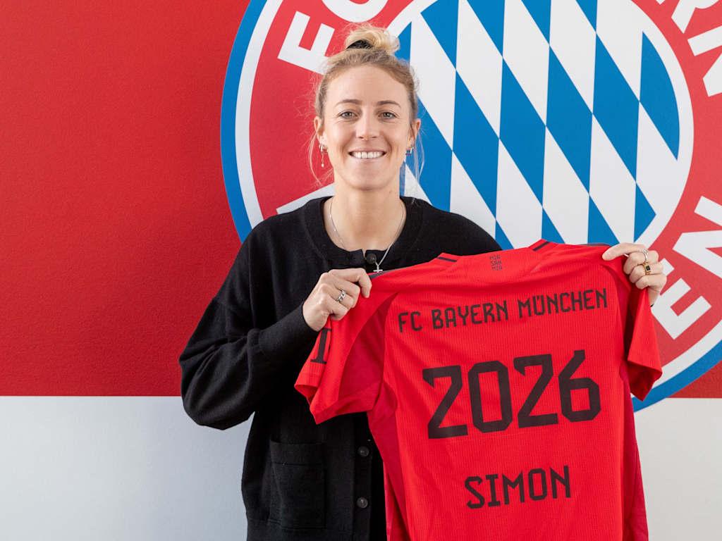 Carolin Simon posiert vor dem FC Bayern Logo mit einem Trikot mit der Rückennummer 2026.