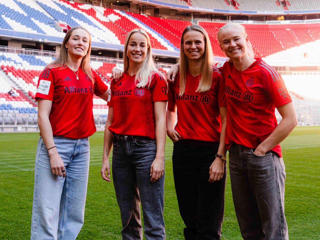 FC Bayern Women's Sydney Lohmann, Giulia Gwinn, Klara Bühl and Pernille Harder posing in FCB jerseys on the pitch in the Allianz Arena.
