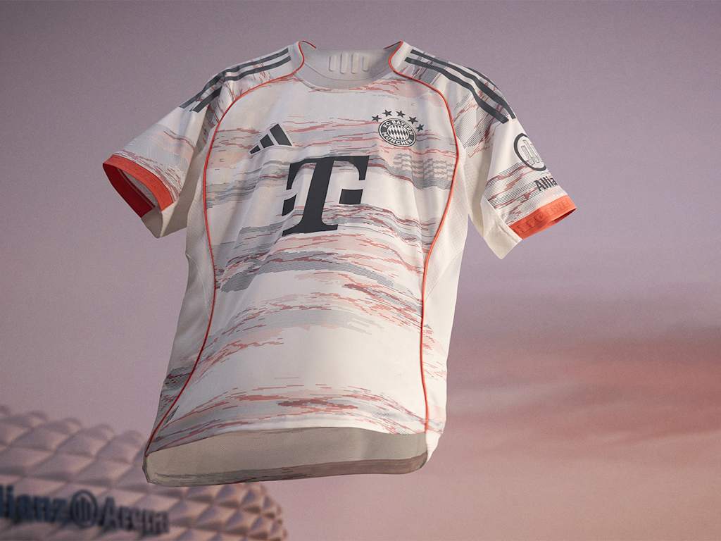 Das neue Auswärtstrikot des FC Bayern für die Saison 2025/26 in Weiß, Grau und leuchtendem Coral schwebt vor der Allianz Arena.