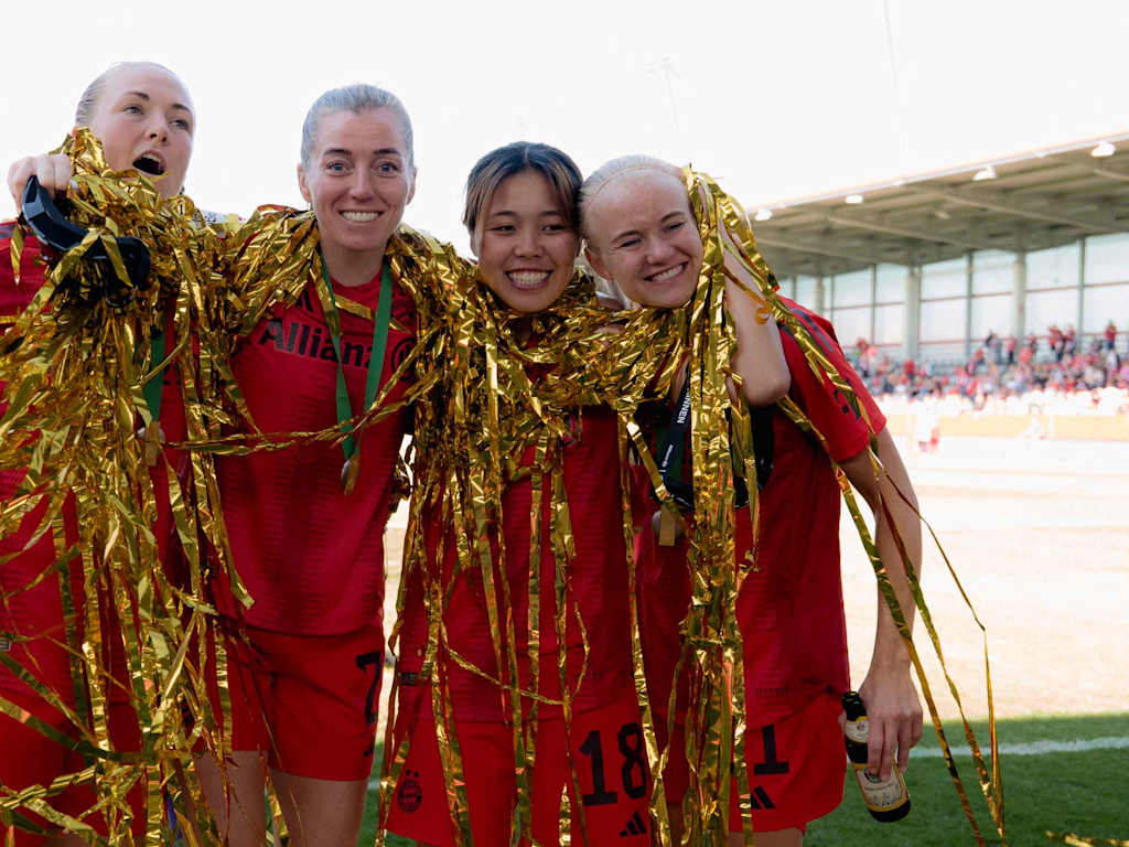 Magdalena Eriksson, Linda Sembrant, Momoko Tanikawa und Pernille Harder von den FC Bayern Frauen stehen Arm in Arm mit Lametta um den Hals auf dem Platz und lächeln in die Kamera.