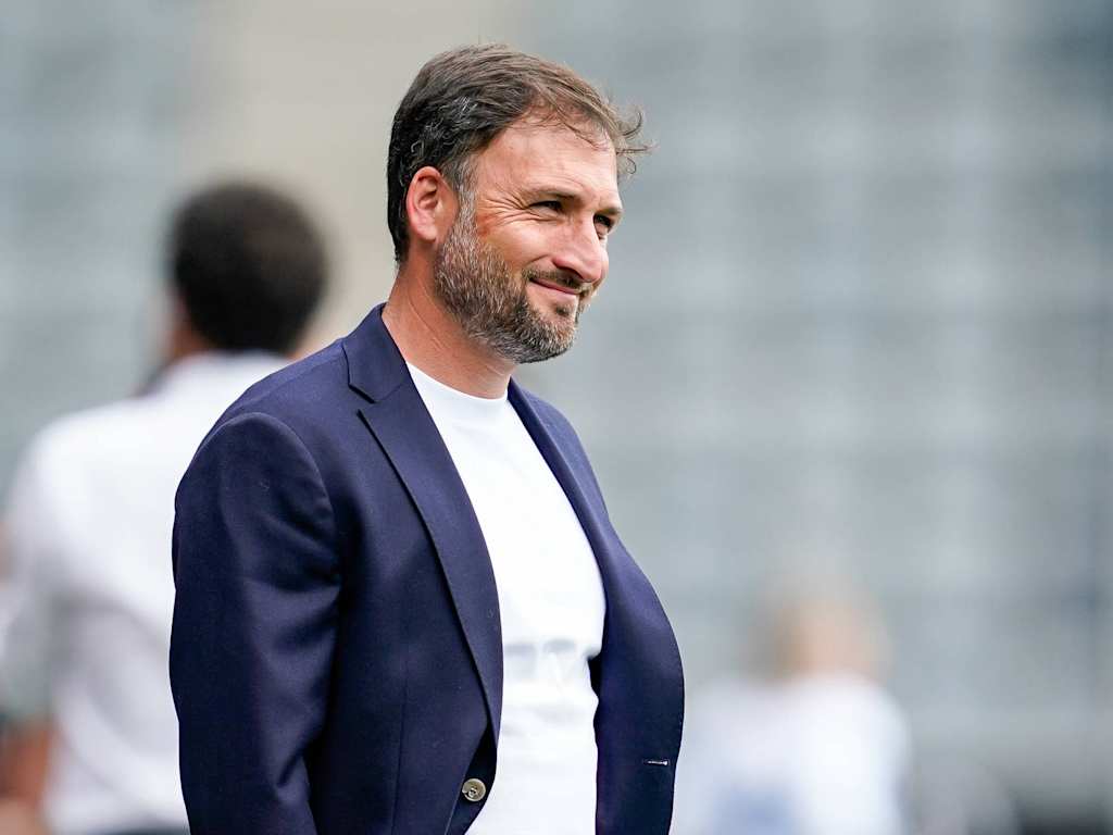 Coach José Barcala standing on the touchline in a suit.