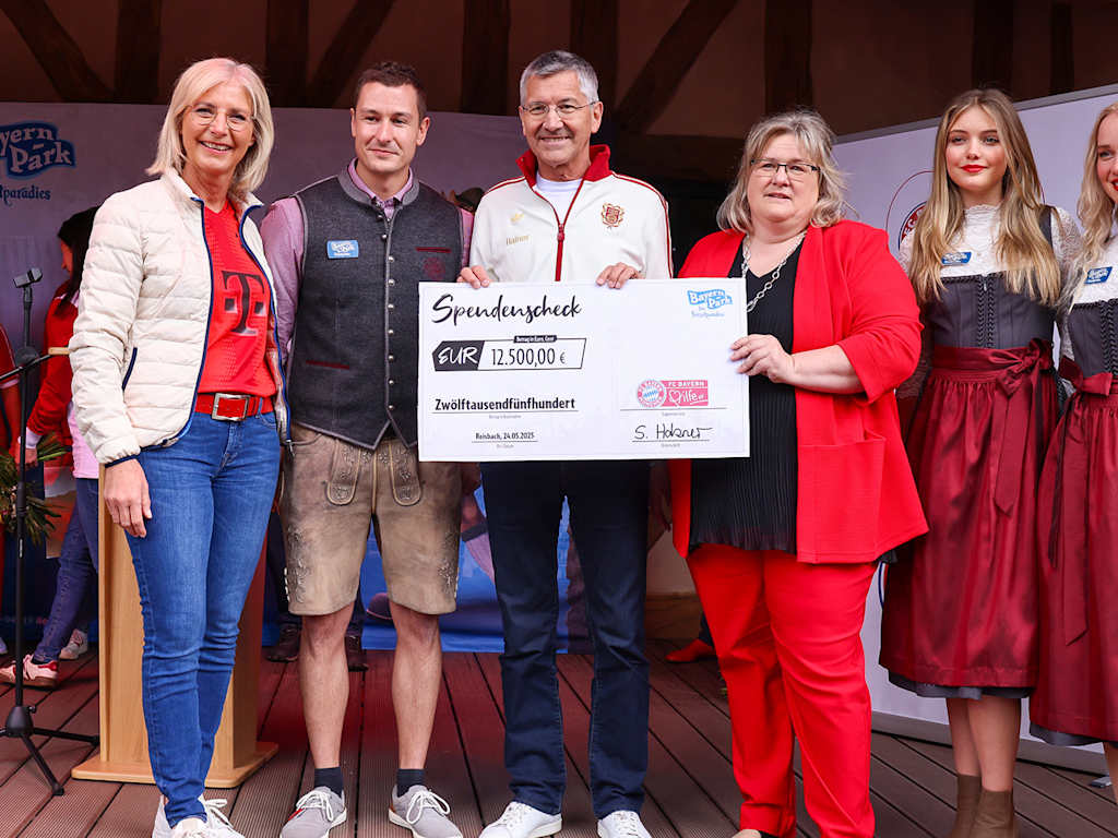 President Herbert Hainer holds up a cheque in a group photo at the fan festival at  Bayern Park