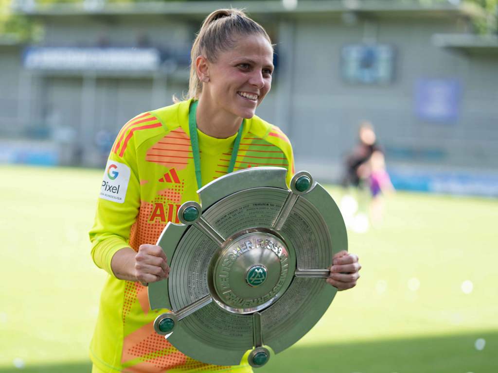 Anna Wellmann hält im gelben Torwart-Trikot die Meisterschale in der Hand und lächelt.