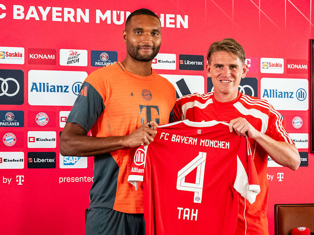 Jonathan Tah und Christoph Freund halten ein FCB-Trikot mit der Rückennummer 4 hoch