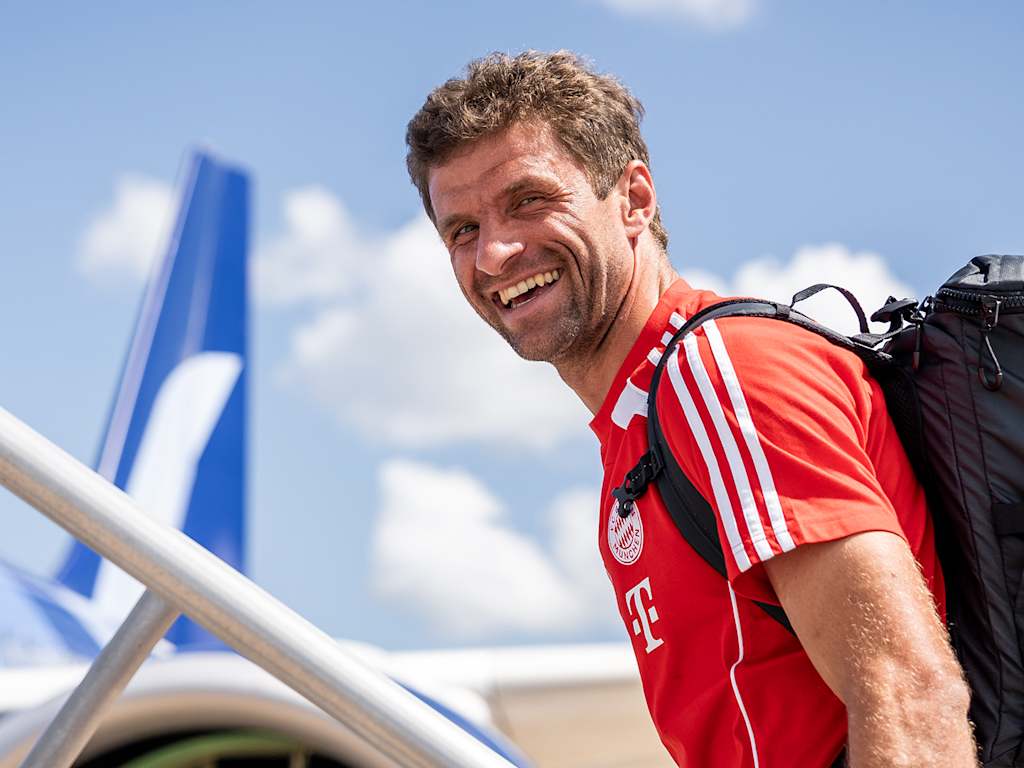 Thomas Müller lacht beim Einsteigen in eine Flugzeug in die Kamera