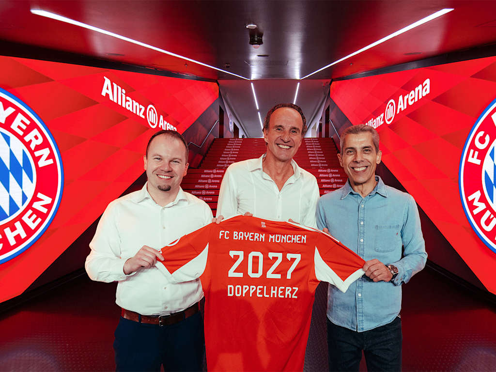 Tim Simonsen, Erich Nobis and Michael Diederich hold up an FC Bayern jersey with the Doppelherz 2027 lettering.