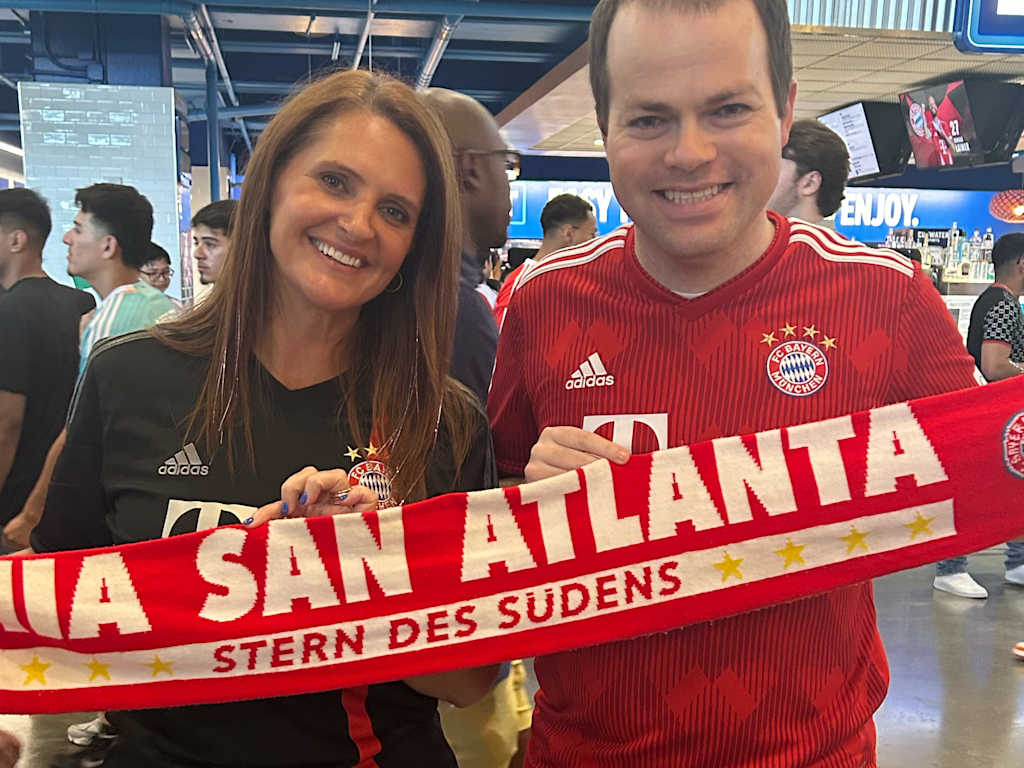 Heather Cooke and Chris Clute wearing Bayern jerseys and a Bayern scarf with the words ‘Mia san Atlanta’ written on it.