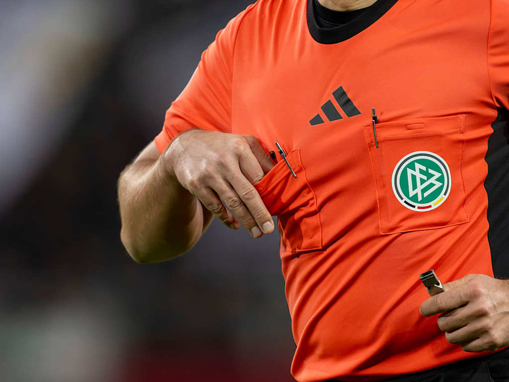 A Bundesliga referee pulls the yellow card out of his breast pocket.