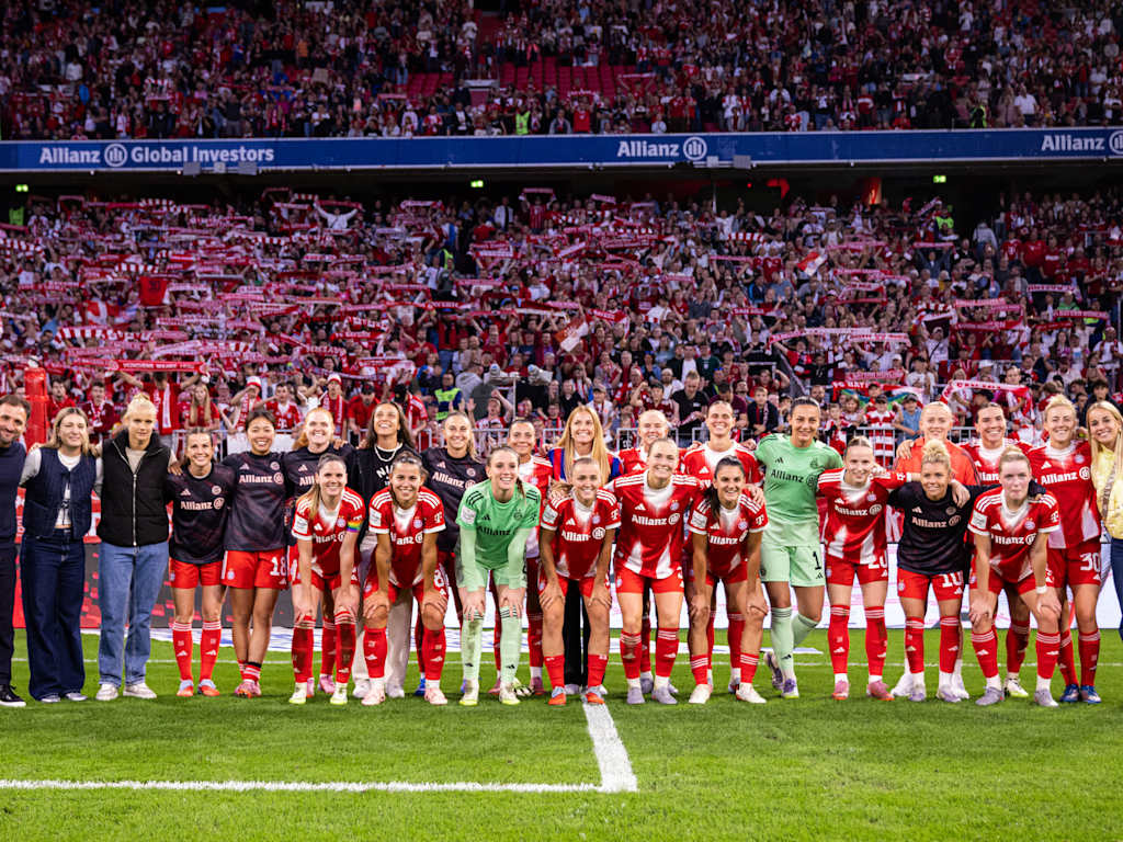 Die FC Bayern Frauen in einem Gruppenfoto vor der Südkurve der Allianz Arena mit Fans im Hintergrund.