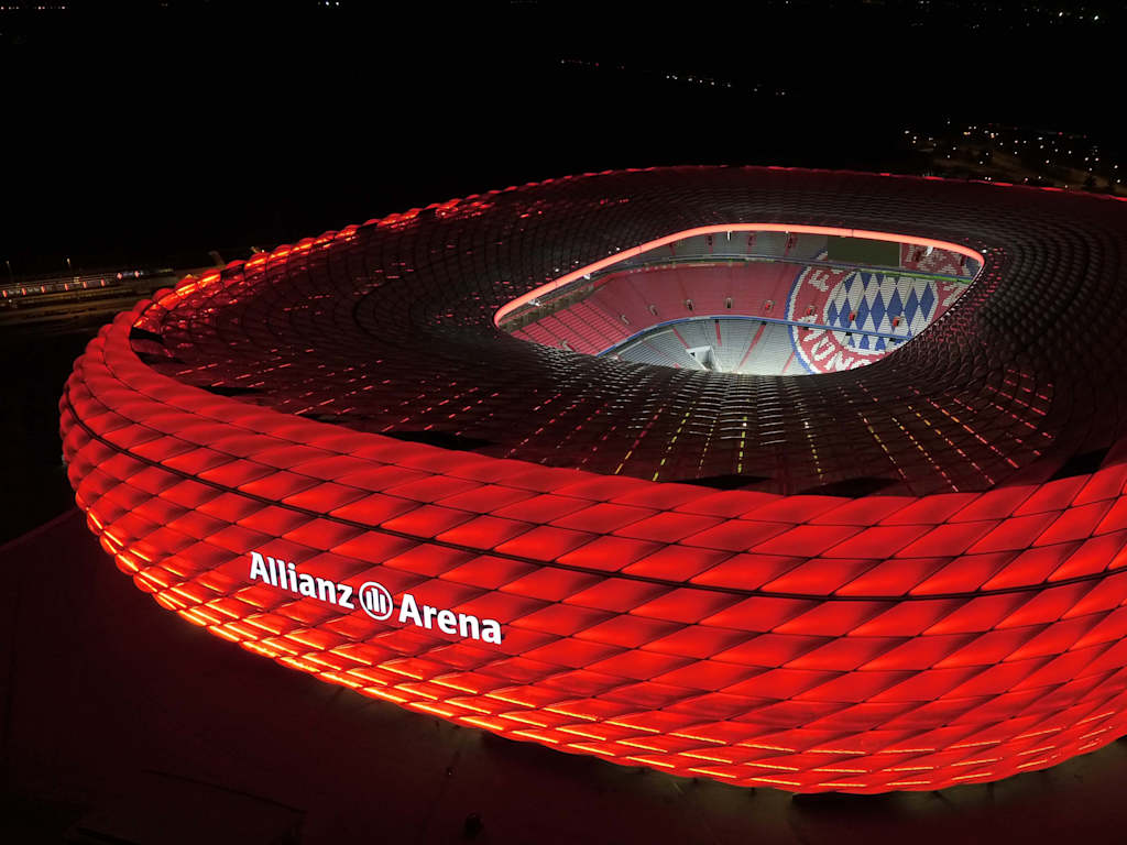 The Allianz Arena lit up in red at night from a birds-eye view.