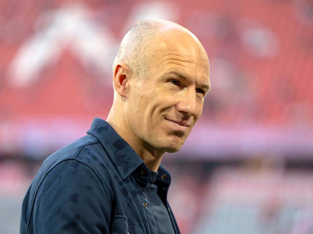 Arjen Robben grins into the camera in a blue shirt.