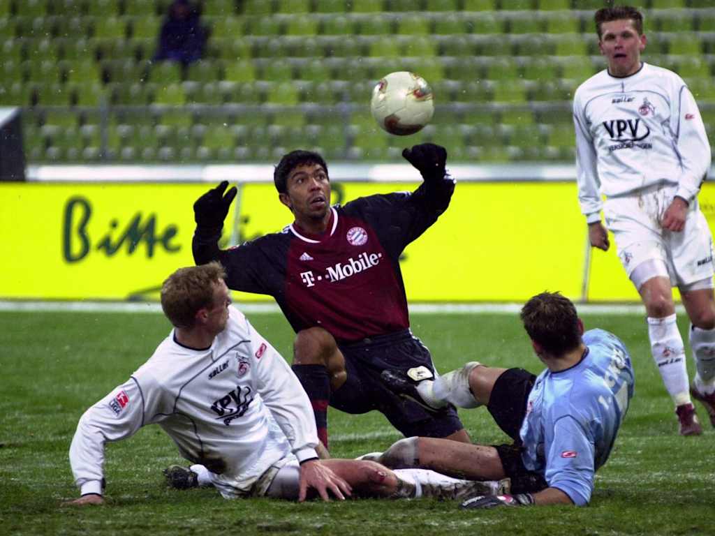 Giovane Elber blickt beim  Pokalspiel gegen Köln am Boden hockend auf dem Ball, umringt von liegenden Kölnern