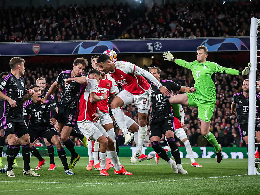 Various FC Bayern players in black and Arsenal players in red go for the ball. Manuel Neuer in green stands in goal.