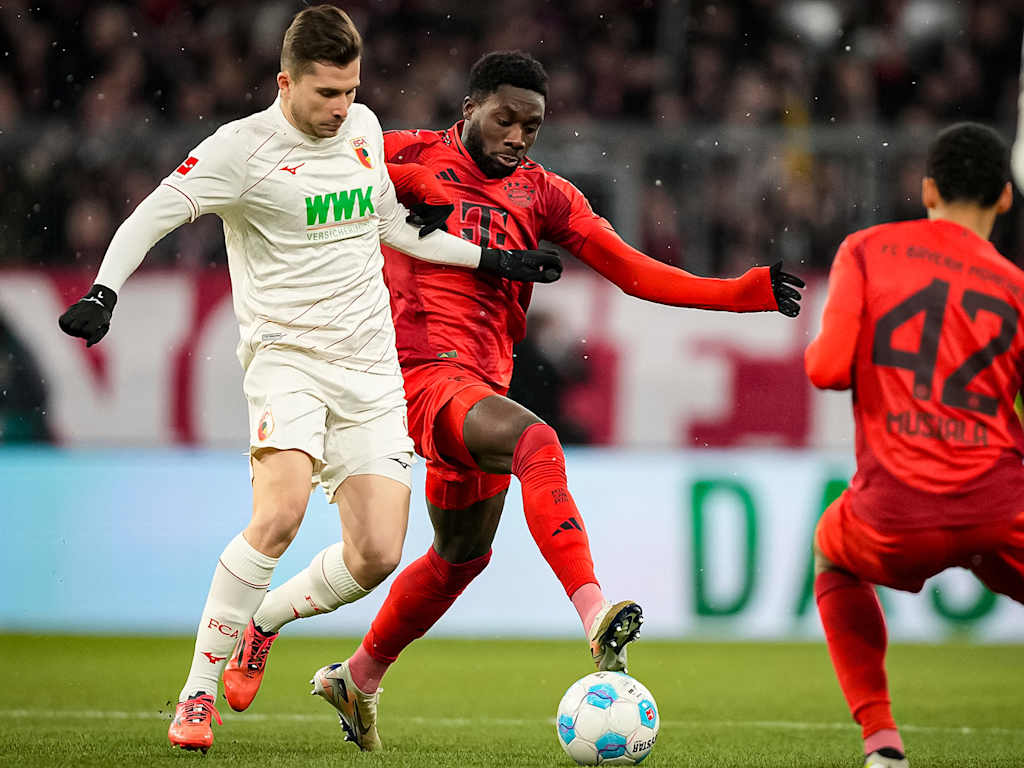 Alphonso Davies in red battling for the ball with an Augsburg player