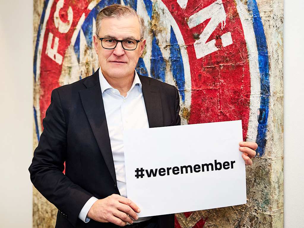 Jan Christian Dreesen, Vorstandsvorsitzender des FC Bayern, zeigt mit ernster Miene ein Banner mit der Aufschrift "weremember" in die Kamera