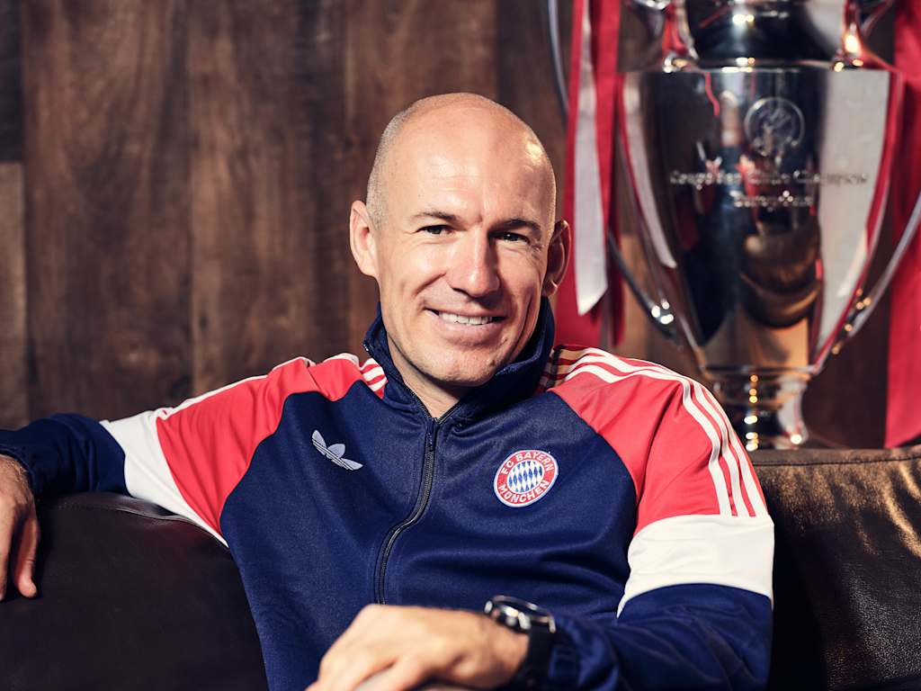 A grinning Arjen Robben in an FC Bayern training jacket on a couch.