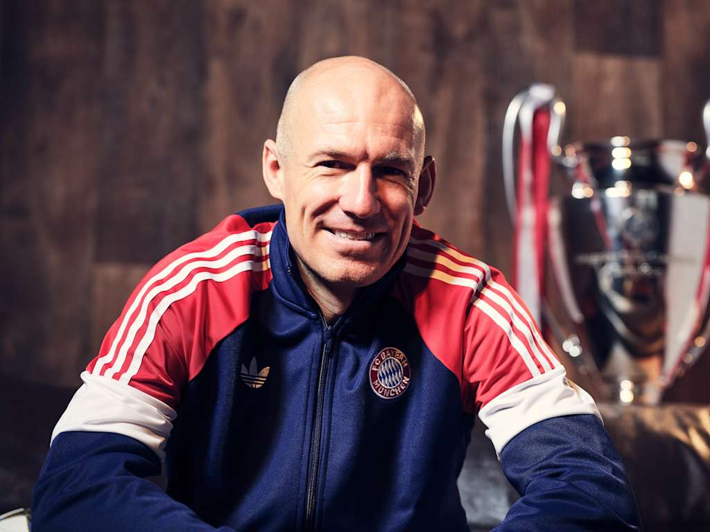 A grinning Arjen Robben in an FC Bayern training jacket on a couch.