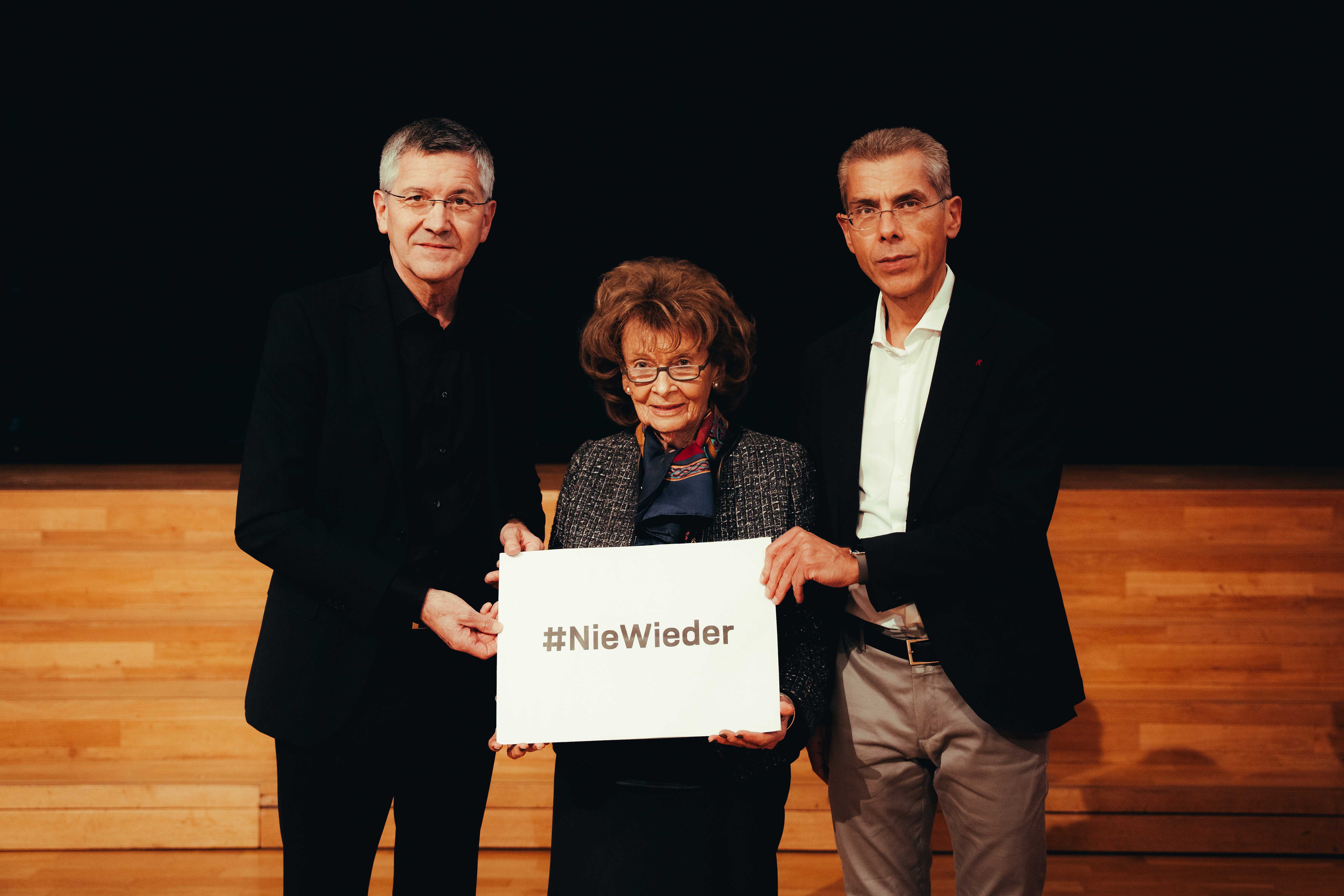 Zum Holocaust-Gedenktag halten Herbert Hainer, Charlotte Knobloch und Michael Diederich die Aufschrift #Niewieder hoch