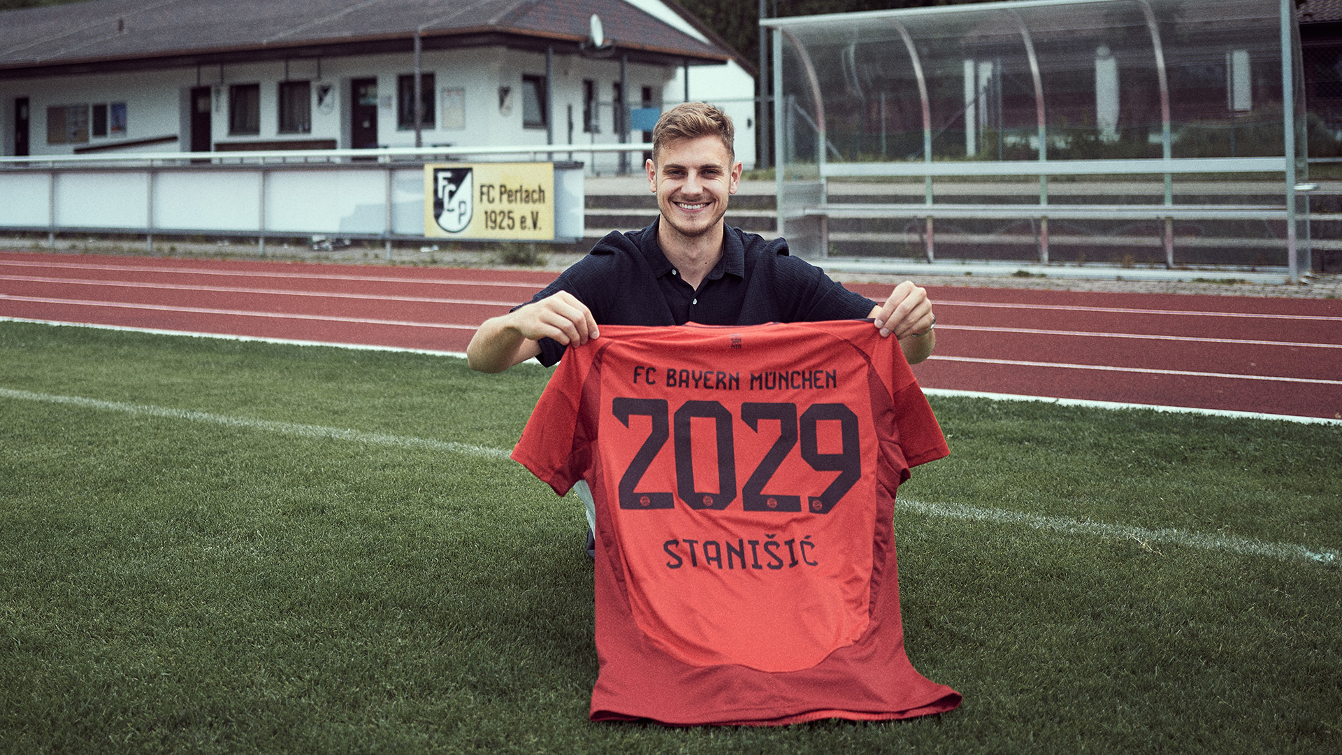 Josip Stanisic holds up an FC Bayern shirt on the pitch of his boyhood club FC Perlach.