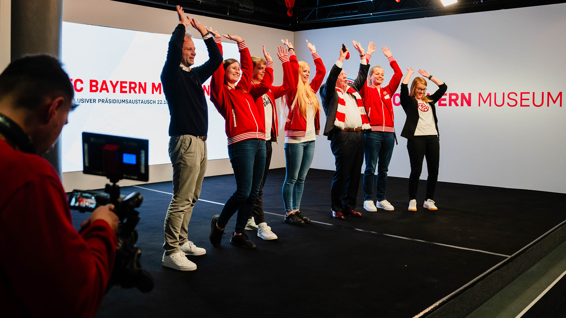 Mitarbeiter machen Laola-Welle beim Austausch mit Ü65-Mitgliedern des FC Bayern