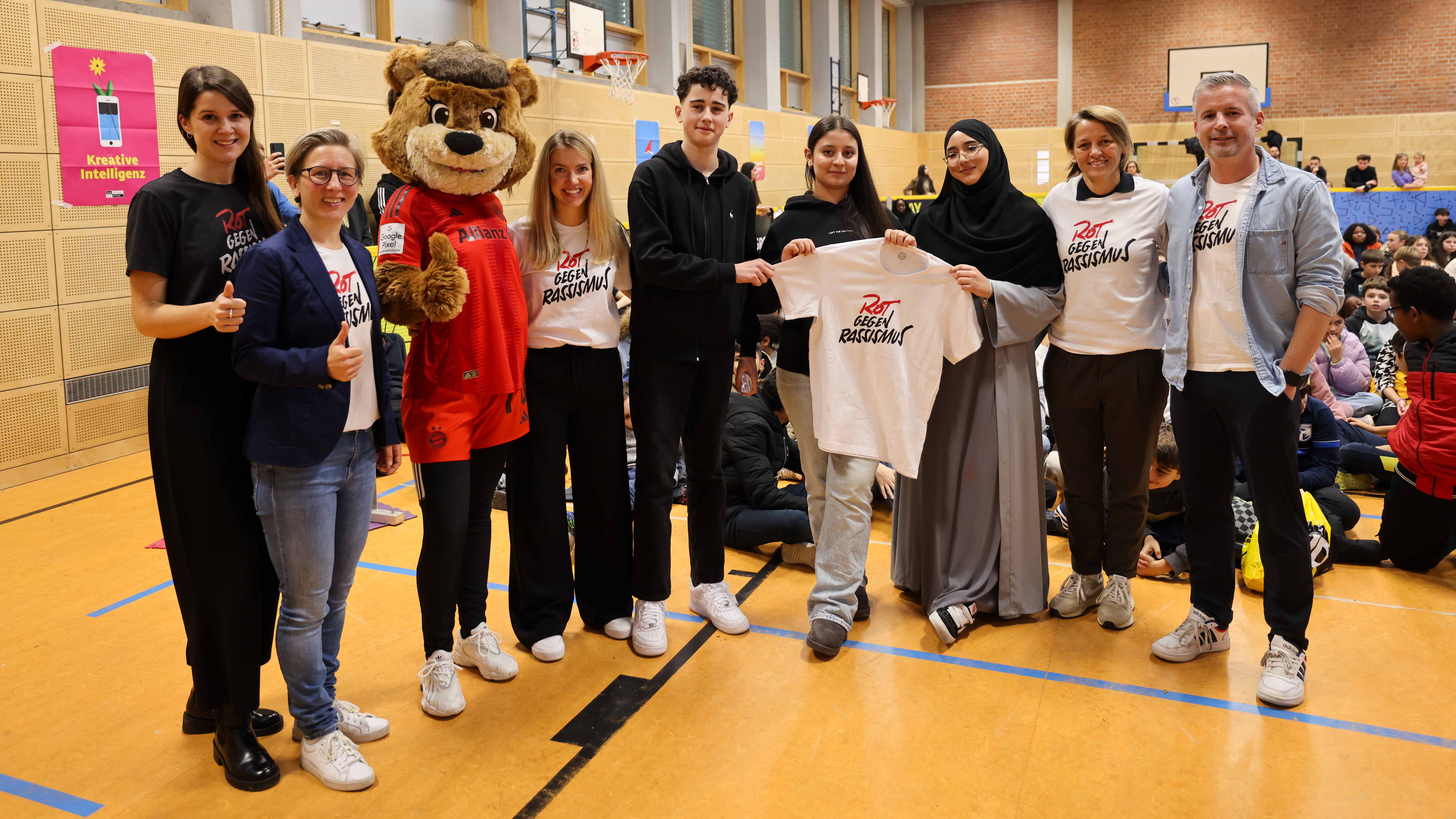 Die Schuelersprecher der Mittelschule an der Perlacher Strasse und die Verantwortlichen des FC Bayern halten ein T-Shirt mit dem Aufdruck 'Rot gegen Rassismus'